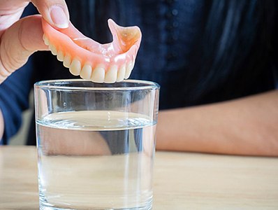 Dentures being dropped into a glass of cleaning solution