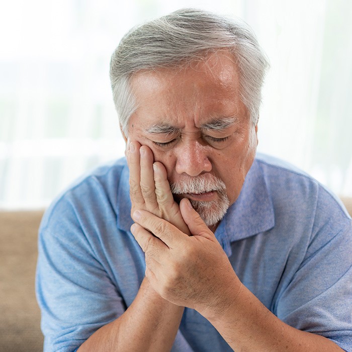  Man sitting on couch with toothache, needing to see emergency dentist in Annandale, VA