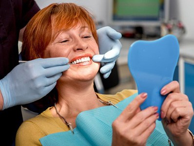 Woman in dental chair looking at her smile after full mouth reconstruction