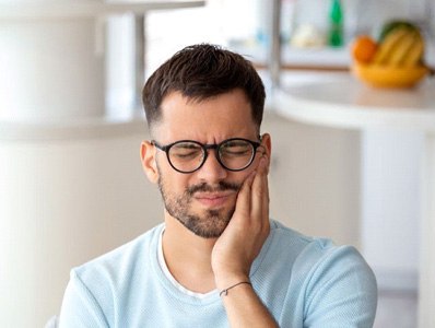 Man wearing pained expression, touching the side of his face