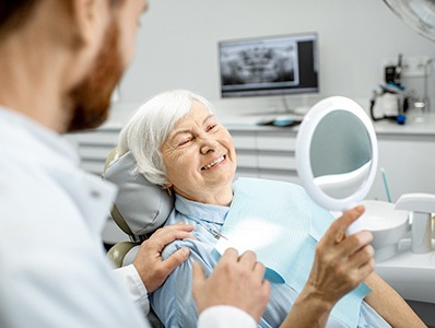 An older woman admiring her new dental implant in a hand mirror