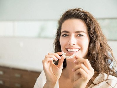Woman smiling and placing an Invislaign clear braces tray