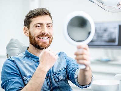 man smiling in mirror after smile makeover in Annandale 