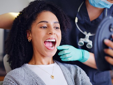 Dentist in green gloves touching woman’s cheek as she looks at mouth in mirror