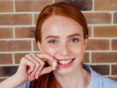 Woman smiling and holding up a tooth after extractions