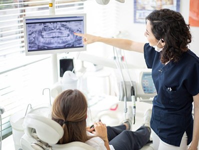 Dentist pointing to digital x-rays to explain T M J disorder symptoms and treatment options