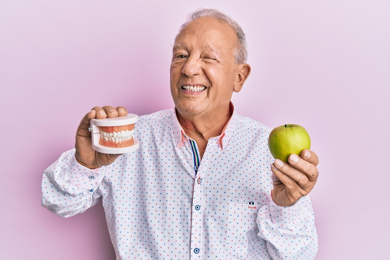 A man holding dentures and a green apple